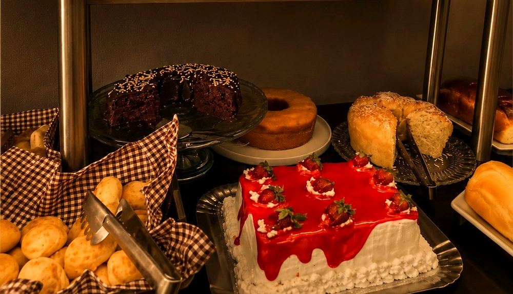 Mesa de café da manhã do Gold Inn Hotel, com pães, bolos e frutas
